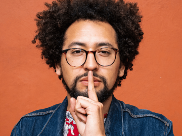 Man holding his finger to his lips to indicate secrecy.